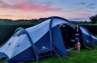 a blue inflatable tent setup in a field on a campsite with a view over the hills and a beautiful sunset