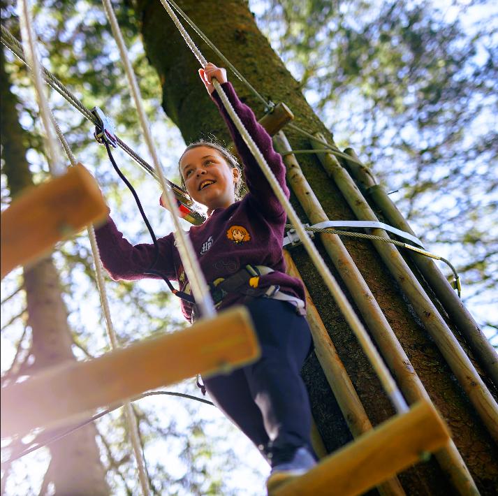 A girl on a high wooden rope walk at go ape treetop adventure plus