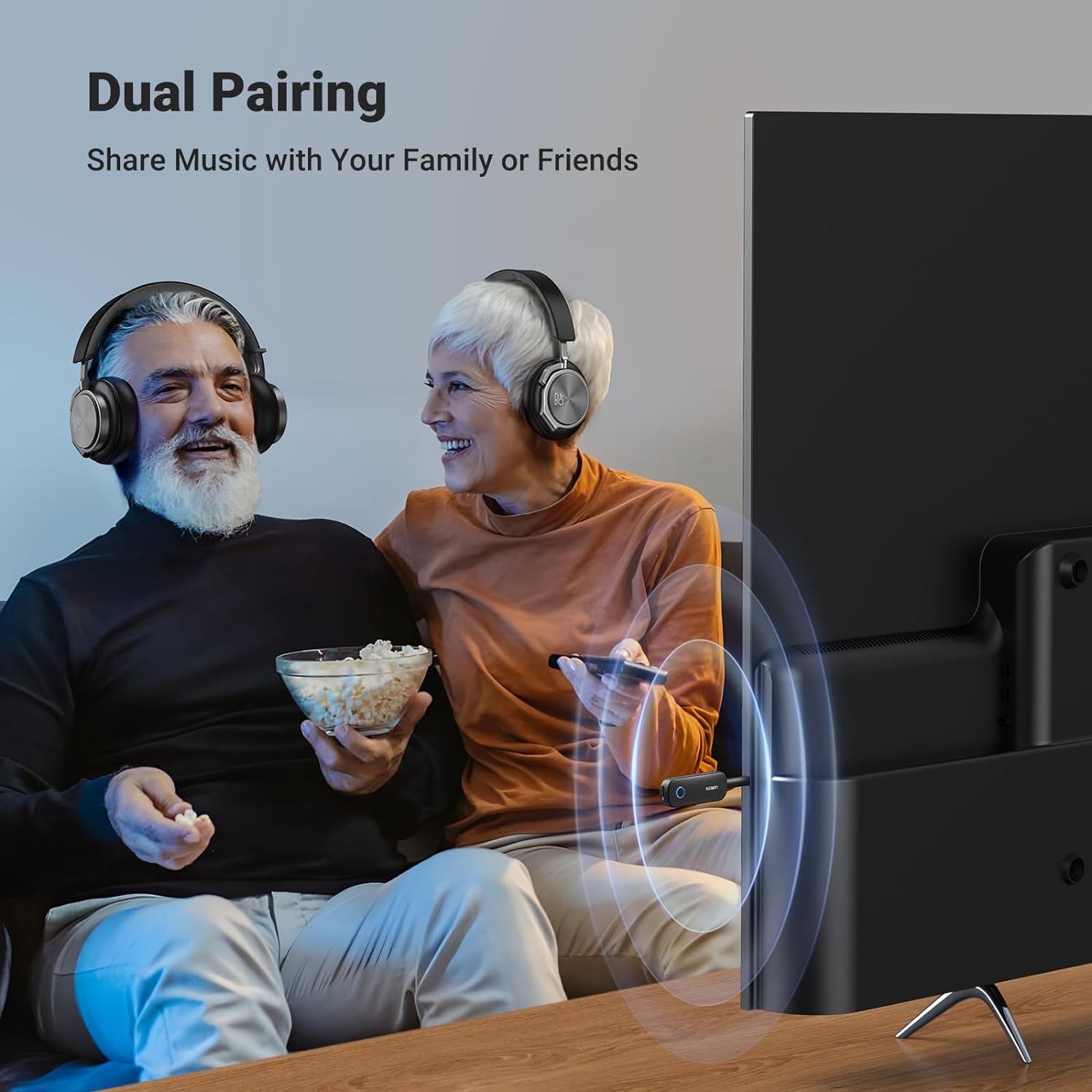 an older couple watching tv with headphones on but sharing the blutooth connection between tv and headphones