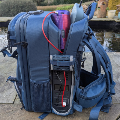 A close up shot of a blue backpack specifically made by Bluetti to hold a power station and your technical equipment to charge gadgets on the go. There are cables visible from equipment to power supply