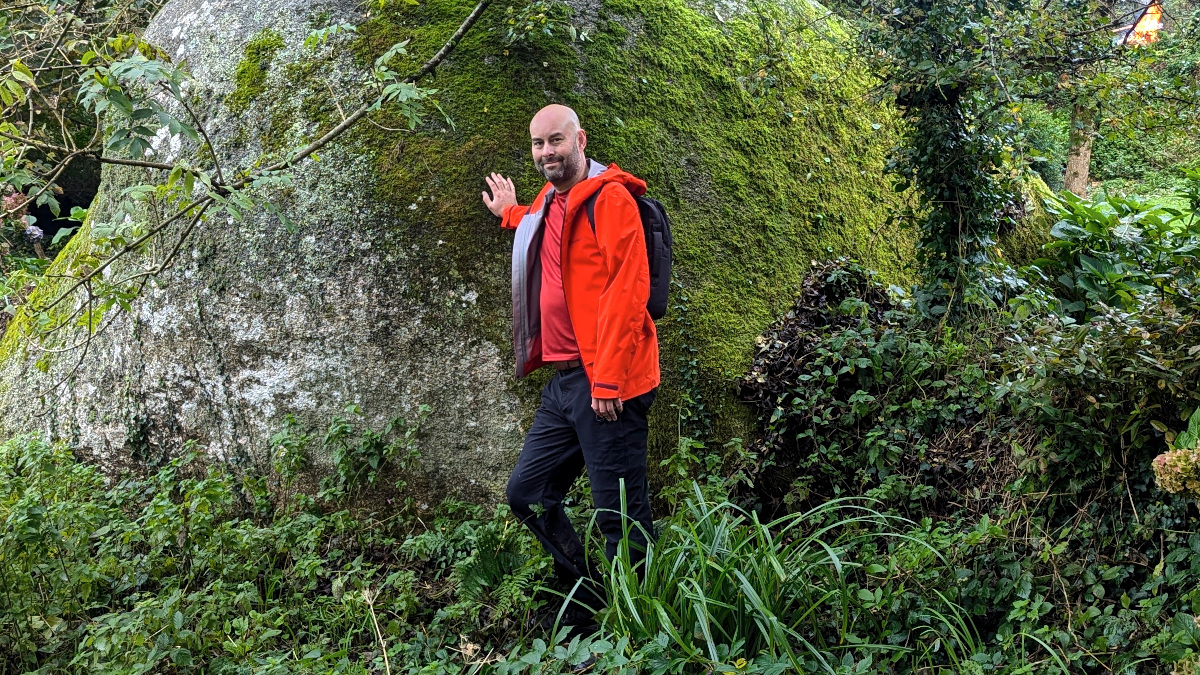 caring for your waterproof jacket. a man with a bright orange waterproof jacket standing holding a massive moss covered bolder