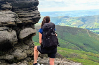 a woman standing looking out over a beautival country side view wearing a quechua mh500 38l backpack in black.
