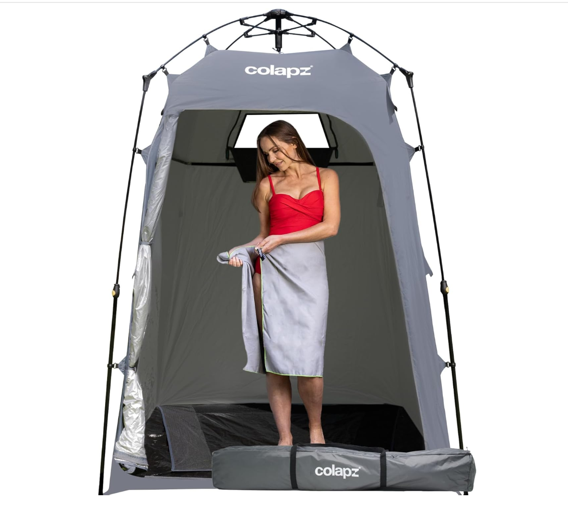 a lady wearing a swimming costume and a towel round her waist stading in a large toilet - shower tent