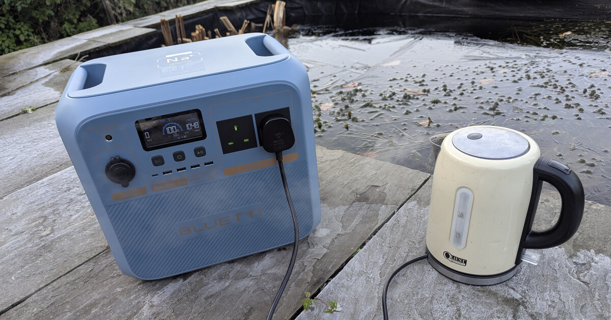 a Bluetti Pioneer Na power station next to a boiling kettle. there is ice and frost on the ground on a winters day